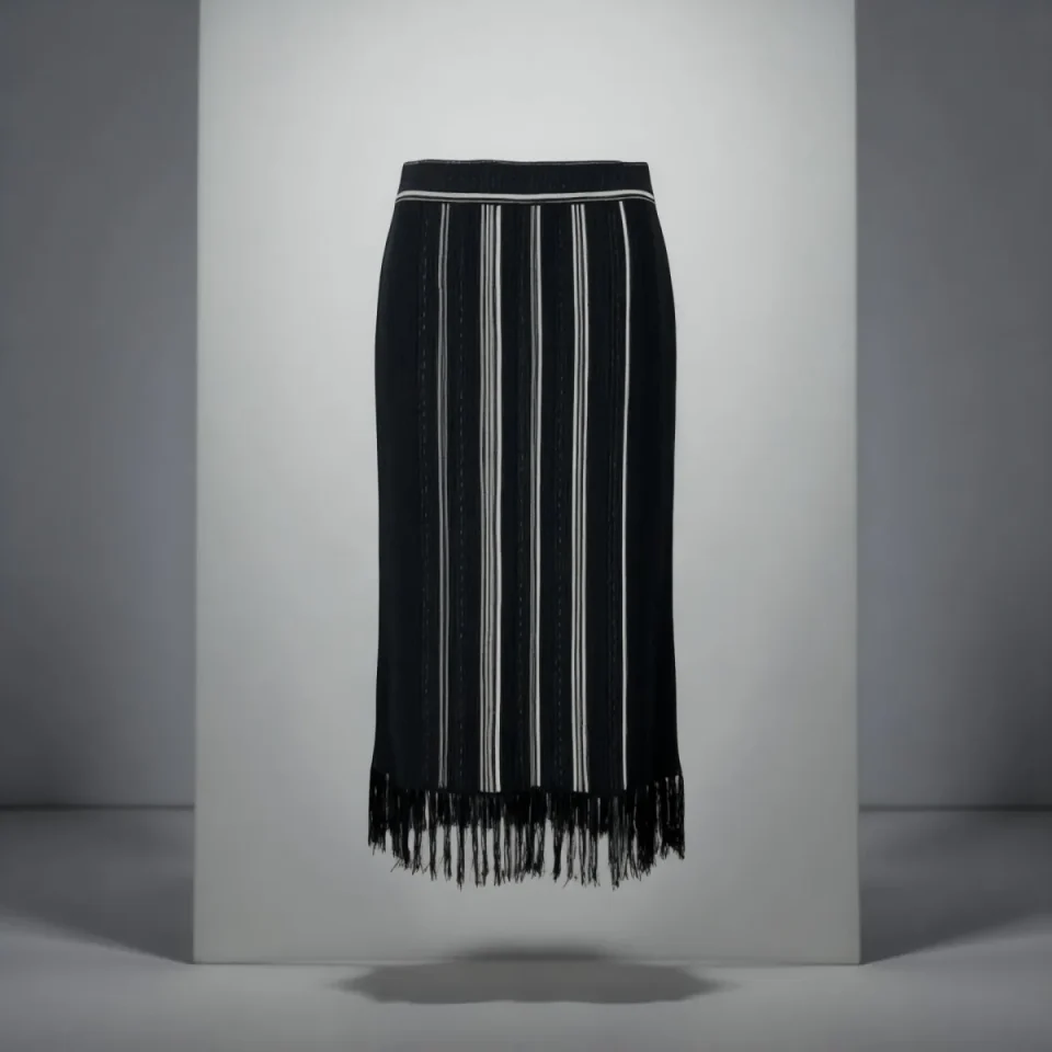 A black fringed knit midi skirt on a plinth against a cool grey studio wall