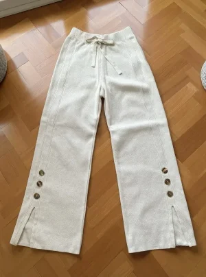 Wide-Leg Knit Trousers with Button Slits — Soft knit wide-leg trousers with side slits and three contrast buttons at the
